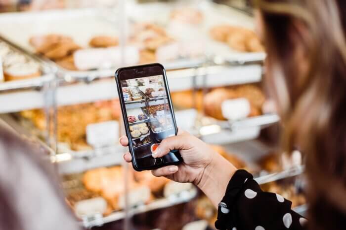 A young woman taking a video of some delicious baked goods in a cafe.