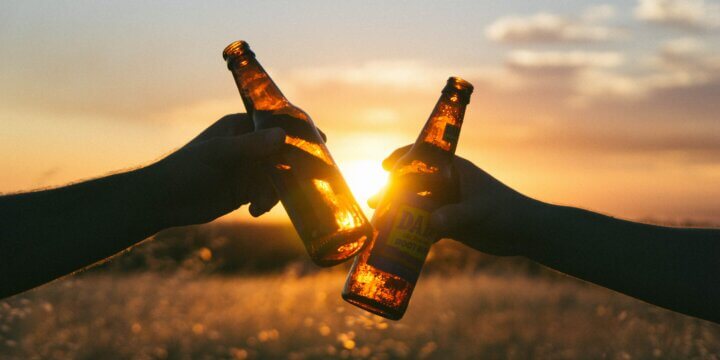 two people holding beer bottles in front of a sunset